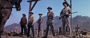 Movie still from “The Magnificent Seven” (1960), directed by John Sturges – A group of men standing on top of a dirt field; Wide shot, Low angle