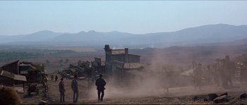 Movie still from “The Magnificent Seven” (1960), directed by John Sturges – Two men are standing in the dirt in front of an old western town; Extreme Wide shot, Low angle