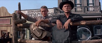 Movie still from “The Magnificent Seven” (1960), directed by John Sturges – Two men standing next to each other on the side of the road; Medium shot, Low angle