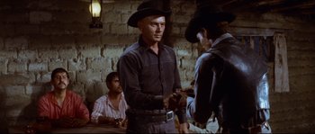 Movie still from “The Magnificent Seven” (1960), directed by John Sturges – A man wearing a cowboy hat is standing in front of two other men; Medium shot, Over the shoulder angle