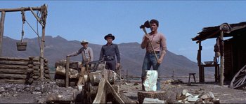 Movie still from “The Magnificent Seven” (1960), directed by John Sturges – A group of men standing next to a pile of wood; Wide shot, Low angle