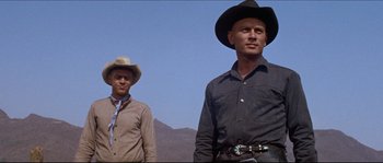 Movie still from “The Magnificent Seven” (1960), directed by John Sturges – Two men standing next to each other on a dirt field; Medium shot, Low angle