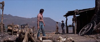 Movie still from “The Magnificent Seven” (1960), directed by John Sturges – Three men standing on a dirt field near a wooden structure; Wide shot, Over the shoulder angle