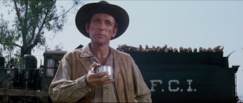 Movie still from “The Magnificent Seven” (1960), directed by John Sturges – A man in a hat holding a cup in his hand; Medium shot, Low angle