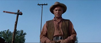 Movie still from “The Magnificent Seven” (1960), directed by John Sturges – A man wearing a cowboy hat standing in front of a power pole; Medium shot, Low angle