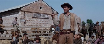 Movie still from “The Magnificent Seven” (1960), directed by John Sturges – A man in a cowboy hat holding a gun in front of a building; Medium shot, Low angle