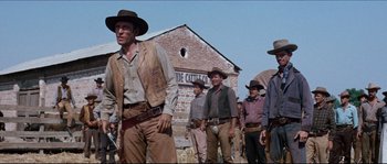 Movie still from “The Magnificent Seven” (1960), directed by John Sturges – A group of men standing next to each other in front of a brick building; Medium shot, Low angle