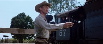 Movie still from “The Magnificent Seven” (1960), directed by John Sturges – A man wearing a cowboy hat standing in front of a train; Medium shot, Low angle