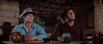 Movie still from “The Magnificent Seven” (1960), directed by John Sturges – Two men in cowboy hats sitting at a dinner table; Medium shot, Low angle