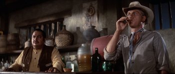 Movie still from “The Magnificent Seven” (1960), directed by John Sturges – A man sitting at a table with a glass of wine; Medium shot, Over the shoulder angle