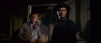 Movie still from “The Magnificent Seven” (1960), directed by John Sturges – Two men standing next to each other in a dark room; Medium shot, Low angle
