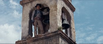 Movie still from “The Magnificent Seven” (1960), directed by John Sturges – A man standing on top of a building next to a bell; Medium shot, Low angle