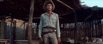 Movie still from “The Magnificent Seven” (1960), directed by John Sturges – A man wearing a cowboy hat standing in front of a wooden structure; Medium shot, Low angle