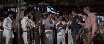 Movie still from “The Magnificent Seven” (1960), directed by John Sturges – A group of men standing next to each other holding drinks; Wide shot, Low angle