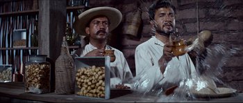 Movie still from “The Magnificent Seven” (1960), directed by John Sturges – Two men sitting at a table with a box of nuts; Medium shot, Low angle