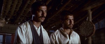 Movie still from “The Magnificent Seven” (1960), directed by John Sturges – Two men standing next to each other in front of a wooden structure; Medium shot, Low angle