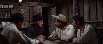 Movie still from “The Magnificent Seven” (1960), directed by John Sturges – A group of men sitting at a table in a room; Medium shot, Over the shoulder angle