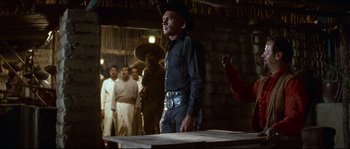 Movie still from “The Magnificent Seven” (1960), directed by John Sturges – A man wearing a cowboy hat stands in front of a group of people; Medium shot, Over the shoulder angle