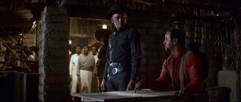 Movie still from “The Magnificent Seven” (1960), directed by John Sturges – A man wearing a cowboy hat standing next to a table; Medium shot, Over the shoulder angle