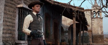 Movie still from “The Magnificent Seven” (1960), directed by John Sturges – A man holding a gun while standing in front of a building; Medium shot, Low angle