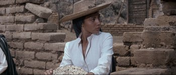 Movie still from “The Magnificent Seven” (1960), directed by John Sturges – A woman wearing a straw hat holding a bowl of nuts; Medium shot, Over the shoulder angle