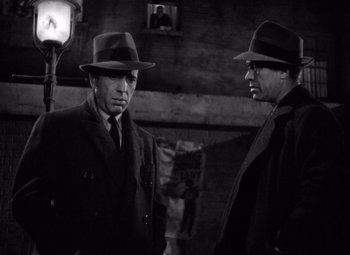 Movie still from “The Maltese Falcon” (1941), directed by John Huston – A couple of men standing next to each other wearing hats; Medium shot, Low angle