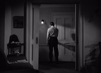Movie still from “The Maltese Falcon” (1941), directed by John Huston – A man standing in front of an open door in a room; Wide shot, Over the shoulder angle