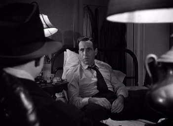 Movie still from “The Maltese Falcon” (1941), directed by John Huston – A black and white photo of a man sitting in a chair; Close Up shot, Over the shoulder angle