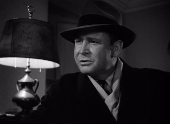 Movie still from “The Maltese Falcon” (1941), directed by John Huston – A man wearing a suit and a hat sitting in front of a lamp; Close Up shot, Low angle
