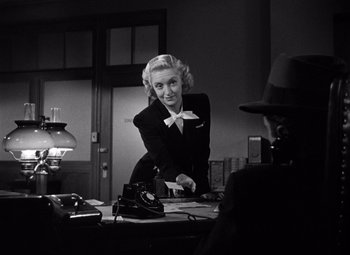Movie still from “The Maltese Falcon” (1941), directed by John Huston – An old photo of a woman posing for a picture in front of a camera; Medium shot, Over the shoulder angle