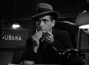 Movie still from “The Maltese Falcon” (1941), directed by John Huston – A black and white photo of a man in a suit and hat eating; Close Up shot, Low angle