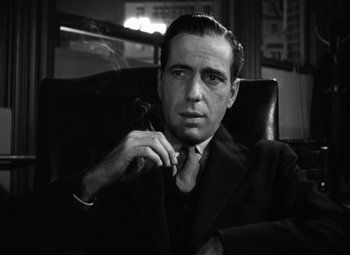Movie still from “The Maltese Falcon” (1941), directed by John Huston – Black and white photograph of a man smoking a pipe; Close Up shot, Low angle