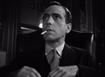 Movie still from “The Maltese Falcon” (1941), directed by John Huston – Black and white photograph of a man smoking a cigarette; Close Up shot, Low angle