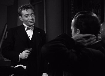 Movie still from “The Maltese Falcon” (1941), directed by John Huston – A black and white photo of a man in a tuxedo holding a drink; Medium shot, Over the shoulder angle