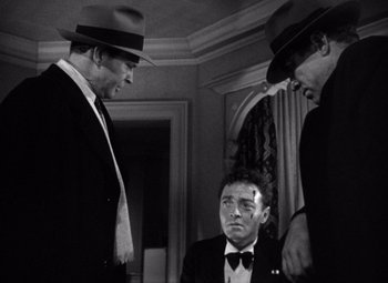 Movie still from “The Maltese Falcon” (1941), directed by John Huston – A man in a suit and tie next to two other men; Medium shot, Low angle