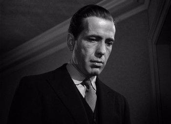 Movie still from “The Maltese Falcon” (1941), directed by John Huston – Black and white photograph of a man wearing a suit and tie; Close Up shot, Low angle