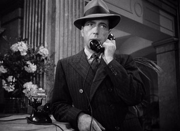 Movie still from “The Maltese Falcon” (1941), directed by John Huston – A man talking on a phone while wearing a suit and hat; Close Up shot, Low angle