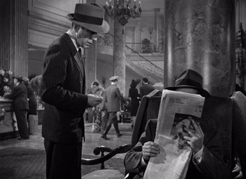 Movie still from “The Maltese Falcon” (1941), directed by John Huston – A man wearing a hat and a suit is looking at a newspaper; Medium shot, High angle