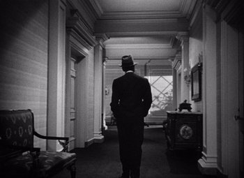 Movie still from “The Maltese Falcon” (1941), directed by John Huston – A black and white photo of a man in a suit and top hat; Wide shot, Over the shoulder angle
