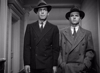 Movie still from “The Maltese Falcon” (1941), directed by John Huston – A couple of men standing next to each other in suits; Medium shot, Low angle