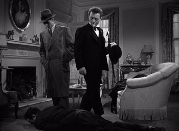 Movie still from “The Maltese Falcon” (1941), directed by John Huston – Two men in suits and hats are standing next to a man laying on the ground; Wide shot, High angle