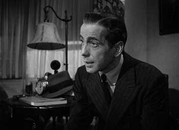 Movie still from “The Maltese Falcon” (1941), directed by John Huston – A man sitting at a desk in a suit and tie; Close Up shot, Low angle