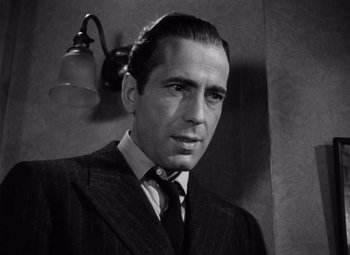 Movie still from “The Maltese Falcon” (1941), directed by John Huston – Black and white photograph of a man wearing a suit; Close Up shot, Low angle