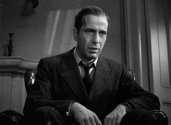 Movie still from “The Maltese Falcon” (1941), directed by John Huston – Black and white photograph of a man wearing a suit and tie; Close Up shot, Low angle