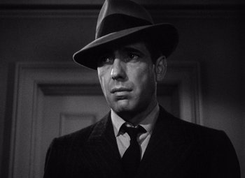 Movie still from “The Maltese Falcon” (1941), directed by John Huston – A black and white photo of a man wearing a suit and a hat; Close Up shot, Low angle