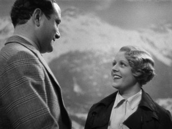 Movie still from “The Man Who Knew Too Much” (1934), directed by Alfred Hitchcock – An older man standing next to an older woman in front of mountains; Medium shot, Low angle