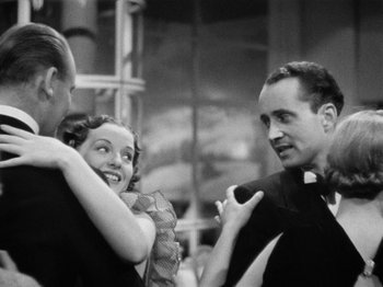 Movie still from “The Man Who Knew Too Much” (1934), directed by Alfred Hitchcock – A black - and - white photo of two men and a woman; Medium shot, Low angle