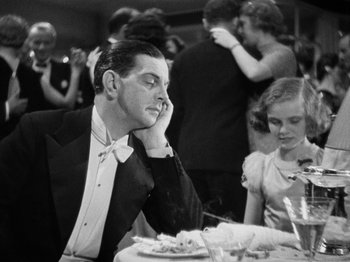 Movie still from “The Man Who Knew Too Much” (1934), directed by Alfred Hitchcock – A black and white photo of a man and a woman at a table; Medium shot, High angle