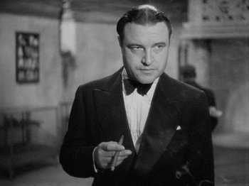 Movie still from “The Man Who Knew Too Much” (1934), directed by Alfred Hitchcock – An old photo of a man in a suit and bow tie; Close Up shot, Low angle