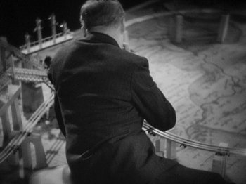 Movie still from “The Man Who Knew Too Much” (1934), directed by Alfred Hitchcock – A black and white photo of a man in a suit; Medium shot, High angle